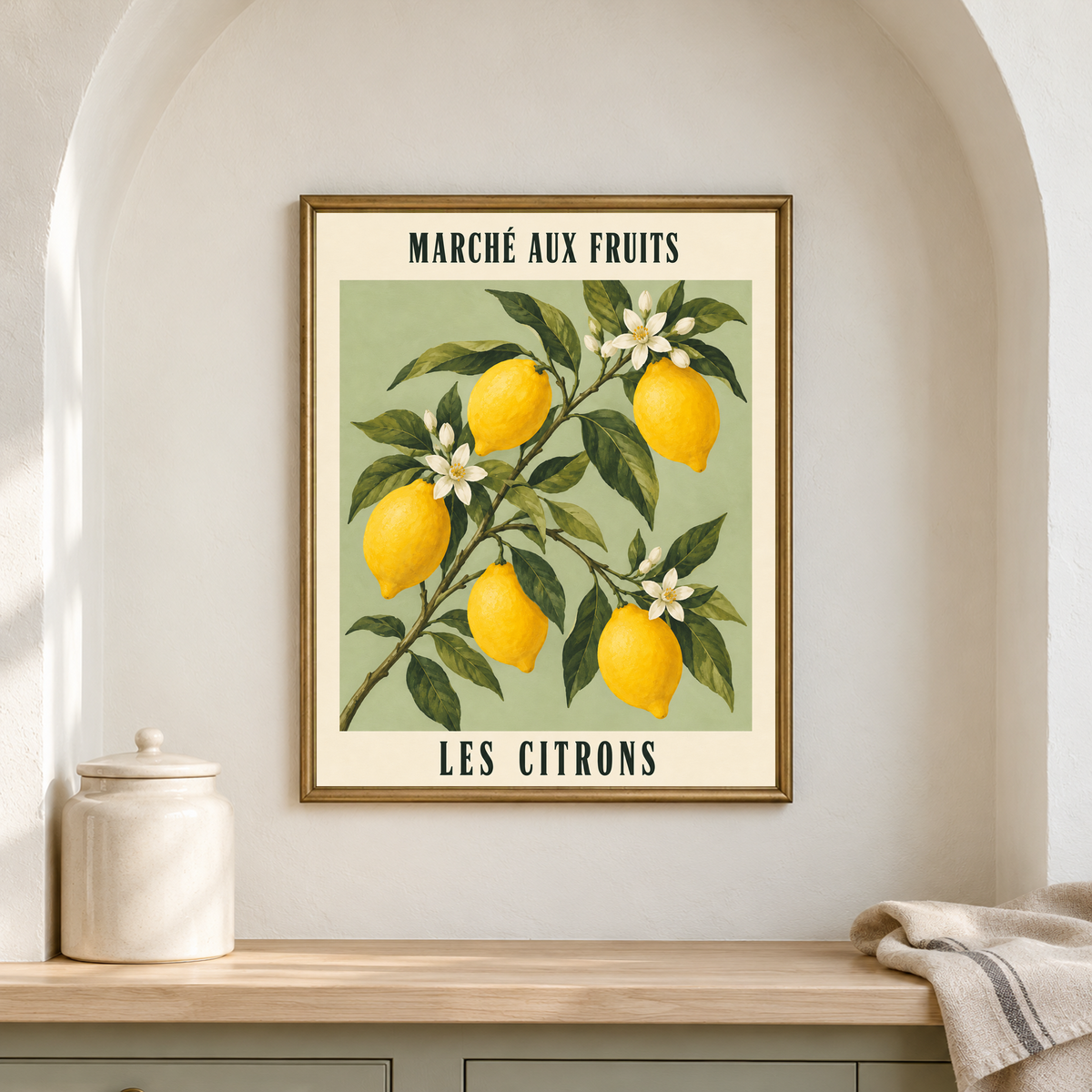 French Lemon Market lemon poster in a brass frame inside a pale arched pantry alcove, above a shelf with a ceramic canister and folded linen.
